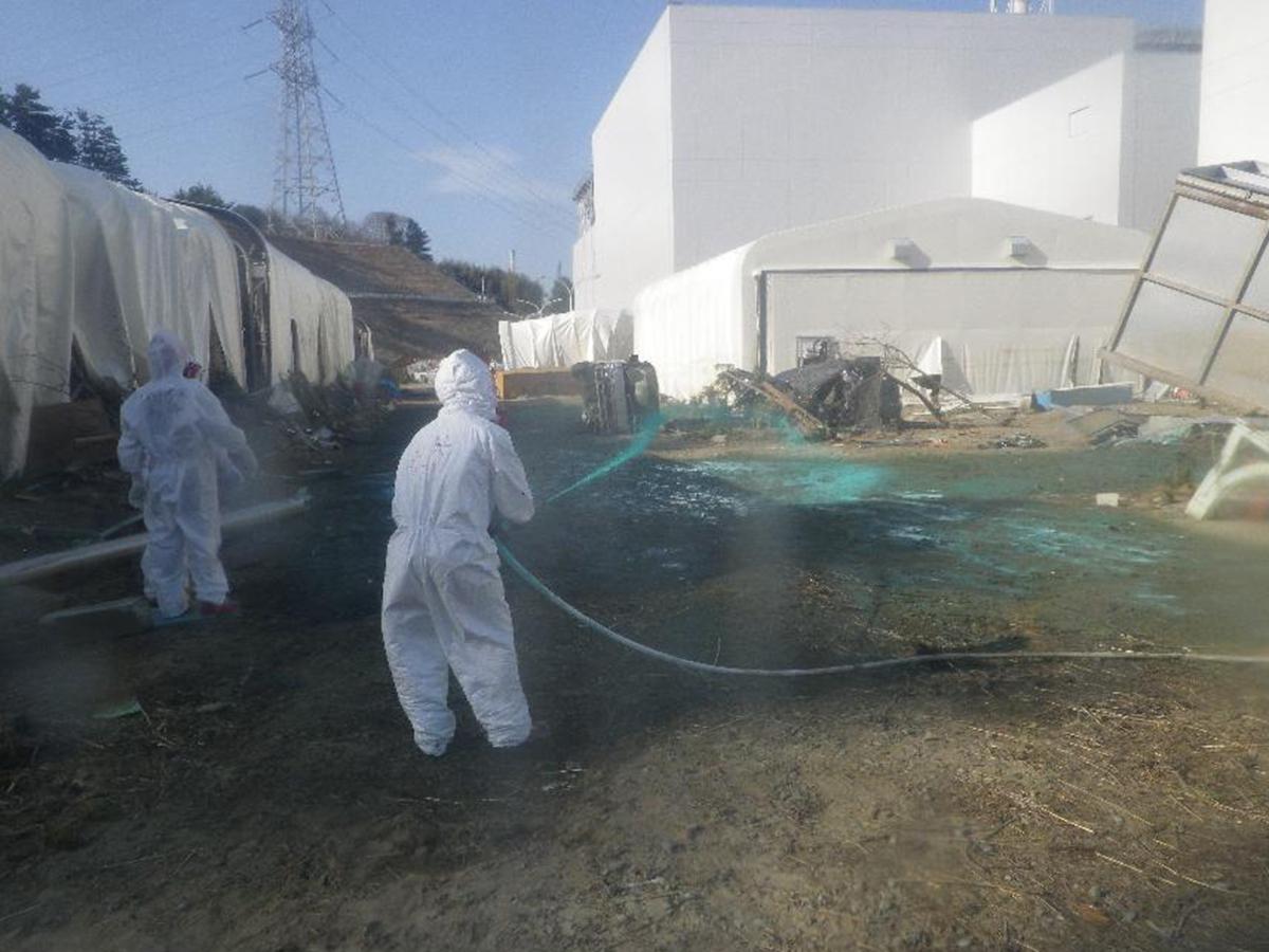 Des employés sprayaient de la résine synthétique sur le sol de la centrale nucléaire accidentée de Fukushima vendredi. [Ho New/Tepco]