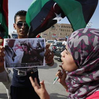 Un homme montre une image du corps de Kadhafi à une femme portant le drapeau libyen. [Abdel Magid al-Fergany]