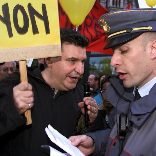 Josef Zisyadis, POP vaudois, est interpele par un policier de la ville de Lausanne au sujet du deplacement de la manifestation contre la fermeture de bureaux de poste, ce mercredi 13 fevrier 2002, a Lausanne. Quelque 400 personnes ont proteste contre la fermeture prevue d'un tiers des bureaux de poste de la capitale vaudoise. Les manifestants ont exige que La Poste renonce a ce projet, comme elle l'a fait pour le bureau de St-Jean a Geneve. (KEYSTONE/Fabrice Coffrini) [Fabrice Coffrini]