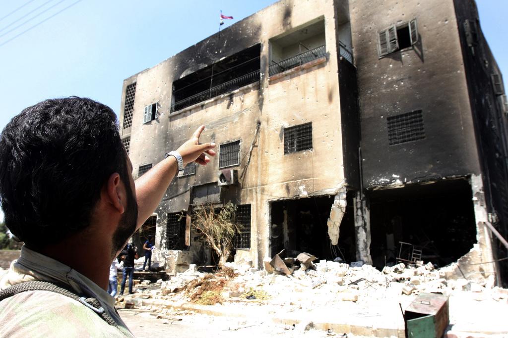 Lors d'un voyage de presse organisé par le gouvernement, un officier syrien pointe du doigt un bureau de police de Hama incendié par les manifestants anti-Assad. [KEYSTONE - Bassem Tellawi]