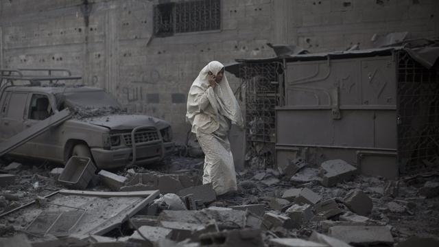 A Gaza City lundi, une femme traverse les décombres d'un bâtiment après un raid israélien. [OLIVER WEIKEN]