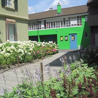 La Rue Neuve avec son école de musique (bâtiment vert). Entre les maisons, les  "jardins de poche" ont remplacé les places de parking. [Valérie Hauert]