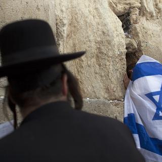 Un juif ultra-orthodoxe et un homme drapé dans le drapeau d'Israël se tiennent face au Mur des Lamentations à Jérusalem. [Darren Whiteside]
