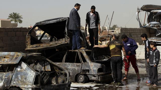 Des Irakiens inspectent les carcasses des véhicules à proximité d'un des attentats survenus dimanche à Bagdad. [Khalid Mohammed]
