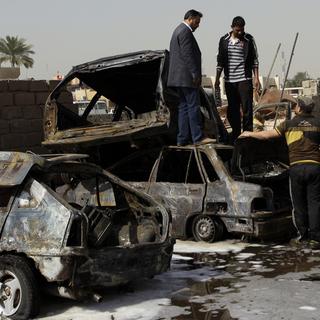 Des Irakiens inspectent les carcasses des véhicules à proximité d'un des attentats survenus dimanche à Bagdad. [Khalid Mohammed]