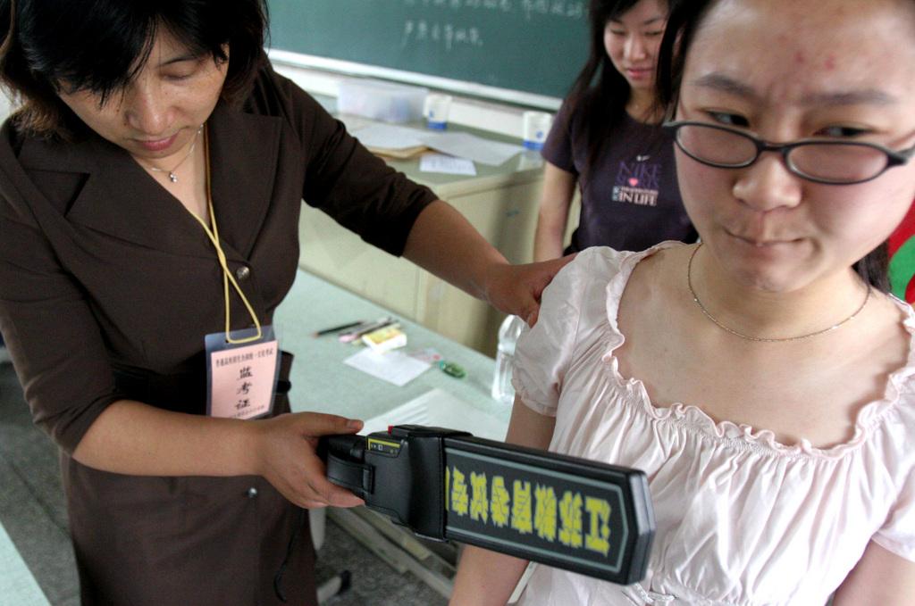 Une enseignante passe au détecteur de métaux une étudiante pour s'assurer qu'elle ne cache pas d'appareils mobiles sous ses habits. [KEYSTONE - AP Photo]