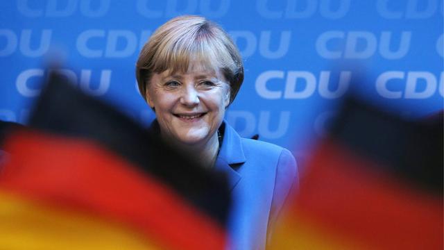 German chancellor Angela Merkel smiles behind German flags at the party headquarters in Berlin, Sunday, Sept. 22, 2013, after the first exit polls have been published. (AP Photo/Michael Sohn) [AP Photo/Michael Sohn]