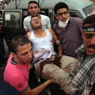 Des partisans de Mohamed Morsi portent un homme blessé dans les heurts avec l'armée. [AP Photo/Khalil Hamra]