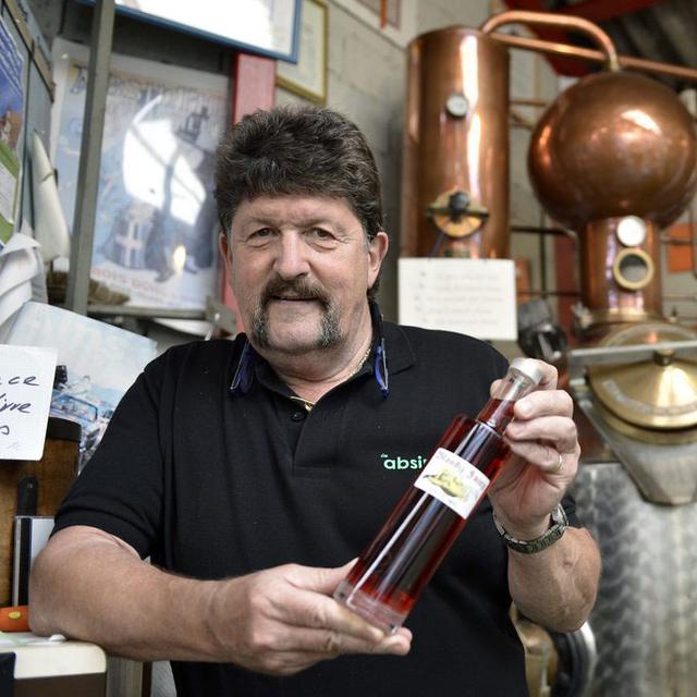 René Wanner devant un alambic, avec une bouteille d'absinthe de sa fabrication. [Martial Trezzini]