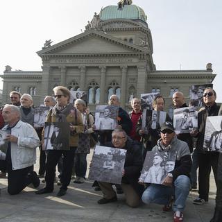 D'anciens enfants placés de force posent avec des photos d'eux, à l'époque, devant le Palais fédéral à Berne en mars 2014. [Keystone - Lukas Lehmann]