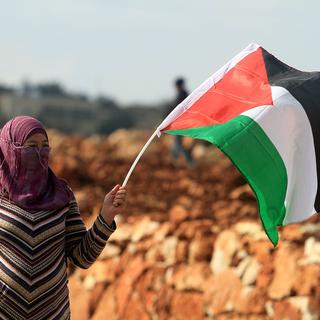 Une femme brandit un drapeau palestinien à Ramallah. [Issiam Rimawi/Anadolu Agency]