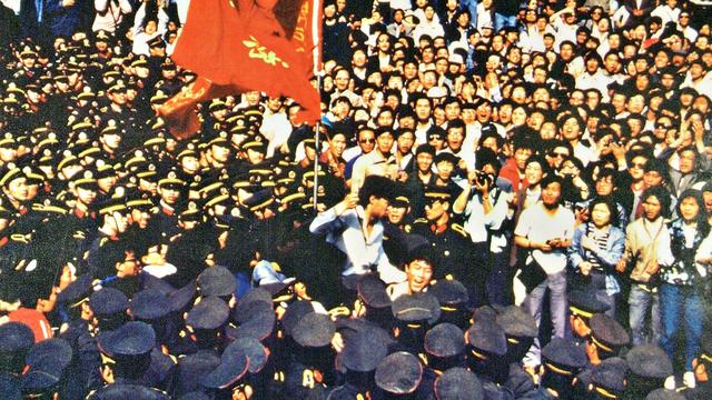 Les étudiants portent Wu'er Kaixi, qui tient le drapeau de son école, contre un "mur de policiers". [www.64museum.org]