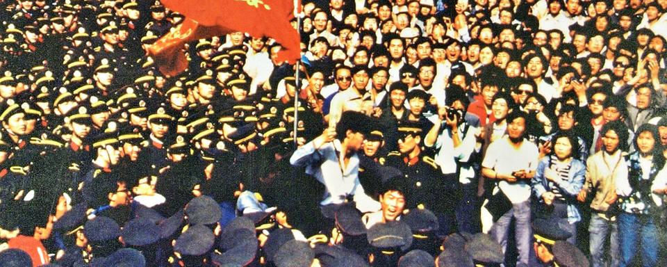 Les étudiants portent Wu'er Kaixi, qui tient le drapeau de son école, contre un "mur de policiers". [www.64museum.org]