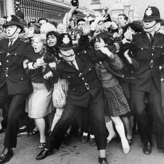 Des fans des Beatles sont contenus par la police devant les grilles du Palais de Buckingham, lors d'une apparition publique du groupe britannique alors qu'il est reçu par la reine, le 26 octobre 1965 à Londres.
