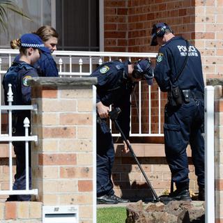 Des policiers passent une maison au détecteur de métaux, ce jeudi 18 septembre à Sydney. [DEean Lewins]
