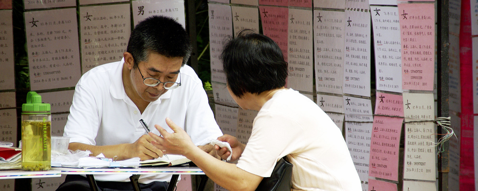 Une mère chinoise parle à un agent, devant un mur de petites annonces. [HUANG Yanning]