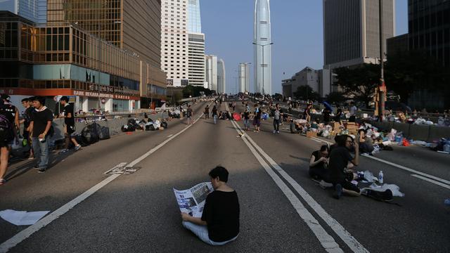 Une femme lit le journal au milieu d'une rue occupée par les manifestants, ce mardi matin à Hong Kong. [Wong Maye-E - AP Photo]