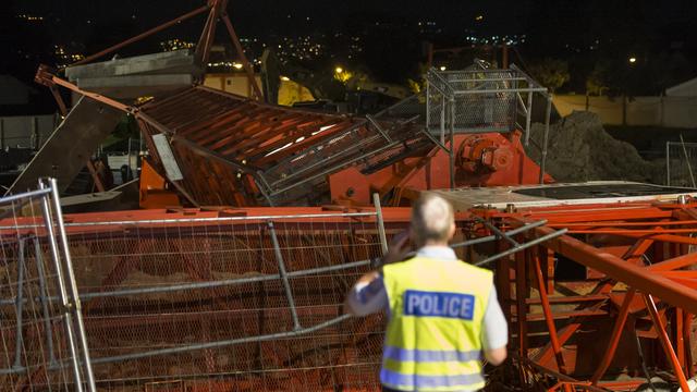 Un policier devant la grue de chantier couchée après sa chute qui a fait un mort et un blessé grave, mercredi 11 juin 2014 a St-Sulpice, Vaud.