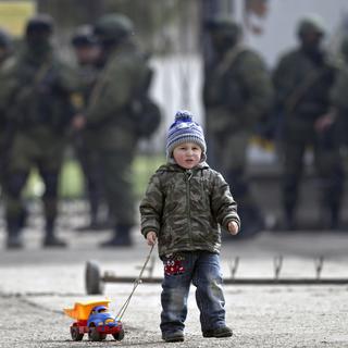 Enfant et son jouet aux abords d'une base militaire ukrainienne à Perevalne (Crimée), surveillée par des soldats pro-russes (arrière-plan). [Vadim Ghirda]