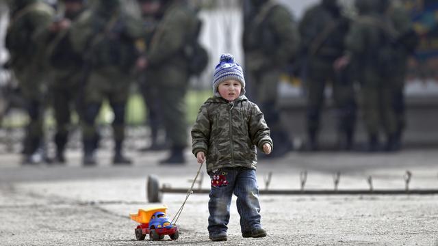 Enfant et son jouet aux abords d'une base militaire ukrainienne à Perevalne (Crimée), surveillée par des soldats pro-russes (arrière-plan). [Vadim Ghirda]