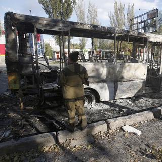 Un rebelle pro-russe examine un bus détruit après un bombardement, le 1er octobre, dans la ville de Donetsk. [Darko Vojinovic]