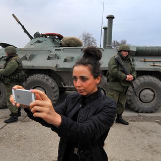 Une femme se prend en photo devant des militaires à Feodosiya, ville côtière de Crimée. [Viktor Drachev]
