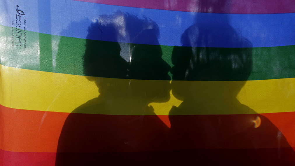 Un couple d'homosexuels s'embrase derrière un drapeau aux couleurs arc en ciel. [AP/Keystone - Dolores Ochoa]