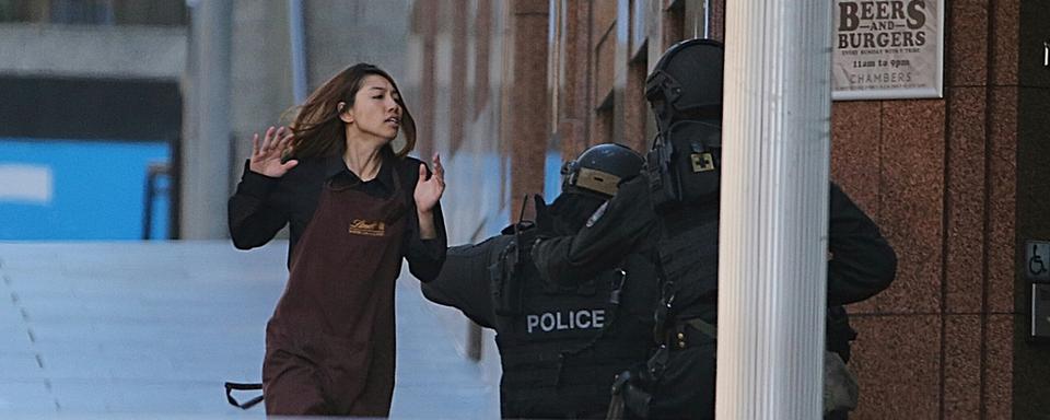 Une employée qui avait été prise en otage vient de s'échapper et est recueillie par des policiers qui assiègent la chocolaterie Lindt de Sydney. [AP Photo/Rob Griffith]