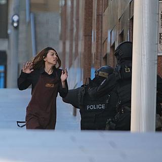 Une employée qui avait été prise en otage vient de s'échapper et est recueillie par des policiers qui assiègent la chocolaterie Lindt de Sydney. [AP Photo/Rob Griffith]