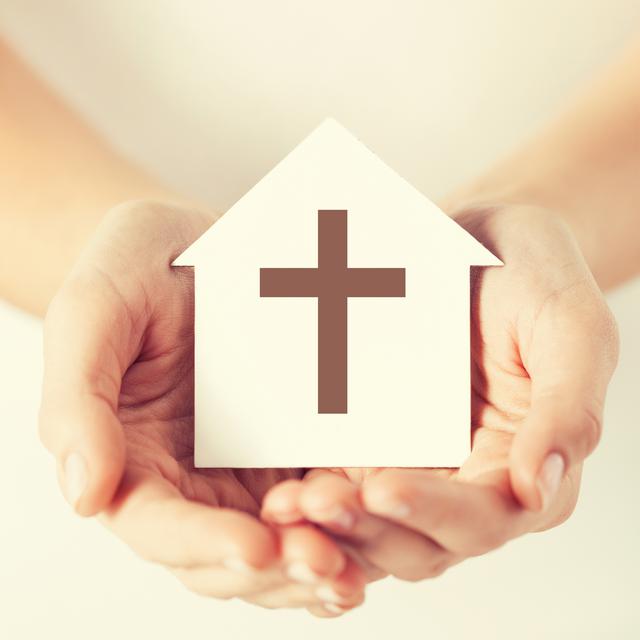 Des mains tenant une maison en papier avec une croix catholique. [Fotolia - Syda Productions]