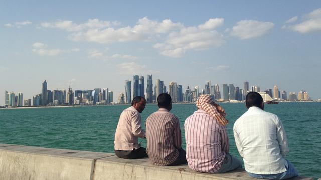 Des hommes assis en bord de mer face à la ville de Doha, capitale du Qatar. [AP/Keystone - Rob Harris]