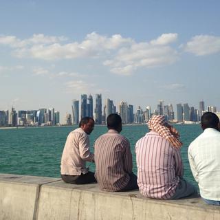 Des hommes assis en bord de mer face à la ville de Doha, capitale du Qatar. [AP/Keystone - Rob Harris]