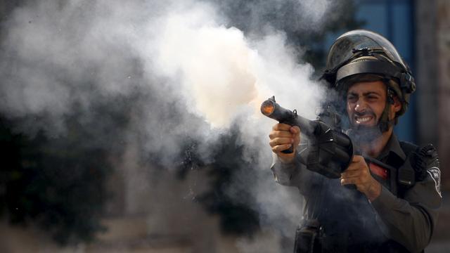 Un policier israélien tire une grenade lacrymogène contre des manifestants à Hébron. [Mussa Qawasma]