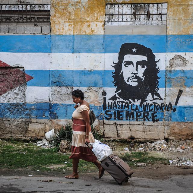 Une femme marchant devant le drapeau cubain et une image du leader révolutionnaire Ernesto Che Guevara à La Havane. [AFP - Yamil Lage]
