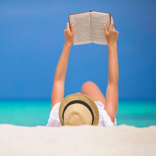 Lire sur le sable, un des plaisirs de l'été. [Fotolia - travnikovstudio]