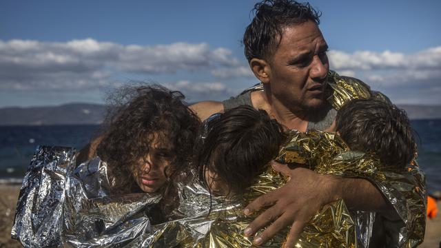 Un homme tient trois enfants enveloppés dans des couvertures thermales, mercredi 28 octobre 2015, sur l'île grecque de Lesbos. [AP Photo/Santi Palacios]