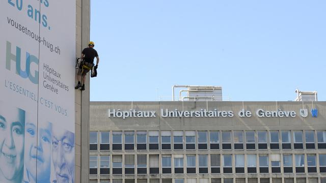 Un alpiniste fixe une toile géante avec des portraits de gens, sur la façade des Hôpitaux universitaires de Genève (HUG) à l'occasion de leurs 20 ans, le 4 juin 2015.