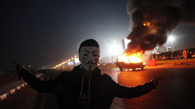 Un supporter masqué du club de Zamalek devant une voiture de police en flammes, dimanche soir au Caire. [EPA/STR]