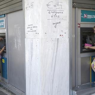 Deux femmes retirent de l'argent à Athènes, des graffitis disent "liberté ou euro". [AP Photo/Keystone - Petr David Josek]