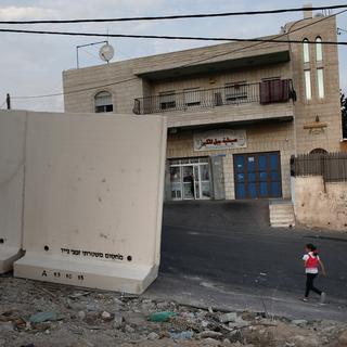 Une jeune fille palestinienne marche à côté du nouveau mur installé par les autorités israéliennes il y a quelques heures.