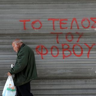 Un Grec passe devant un slogan qui clame "la fin de la peur" à Athènes. [NurPhoto/AFP - Panayiotis Tzamaros]