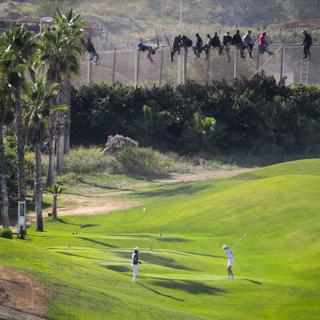 Joueurs de golf observés par des migrants africains. Enclave espagnole de Melilla en Afrique du Nord, le 22 octobre 2014. [Prodein / AFP - José Palazon Osma]
