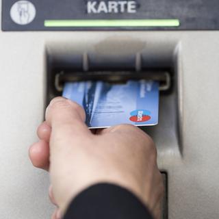 Un client insère une carte bancaire dans un distributeur de billets. [Keystone - Christian Beutler]