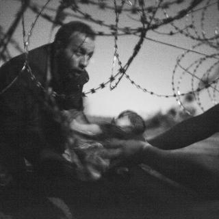 Un homme passe un bébé sous les barbelés à la frontière entre la Serbie et la Hongrie, à Röszke, Hongrie, le 28 août 2015. Photo primée au World Press Contest 2016. [Keystone - Warren Richardson]