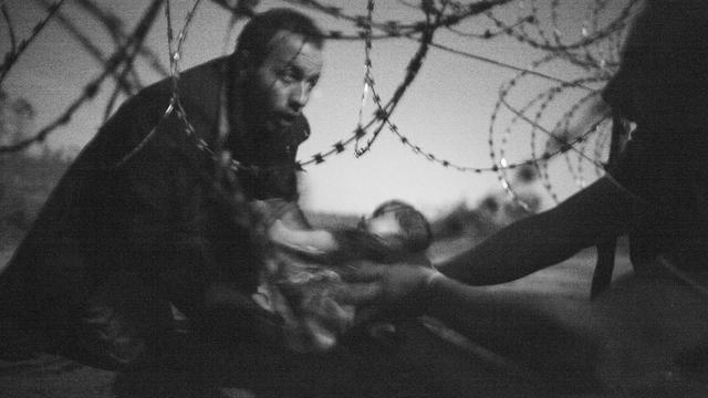 Un homme passe un bébé sous les barbelés à la frontière entre la Serbie et la Hongrie, à Röszke, Hongrie, le 28 août 2015. Photo primée au World Press Contest 2016. [Keystone - Warren Richardson]