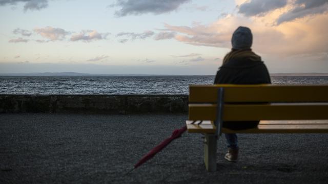 Une femme assise sur un banc face au lac de Constance. [Keystone - Gian Ehrenzeller]