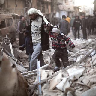 Un homme marche avec des enfants dans les ruines de Ghouta, dans l'est de la Syrie. [Save the Children via AP]
