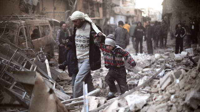 Un homme marche avec des enfants dans les ruines de Ghouta, dans l'est de la Syrie. [Save the Children via AP]