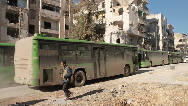 Homme armé passant à côté de bus servant à l'évacuation de civils et de rebelles à Alep-Est jeudi. [EPA/Keystone - Ghth Sy]