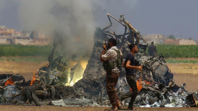 Des hommes inspectent la carcasse encore en feu de l'hélicoptère russe abattu lundi dans le nord-ouest de la Syrie. [Reuters - Ammar Abdullah]